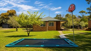 Een achtertuin met een trampoline, een basketbalveld en een huis.