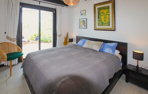 A bedroom with a large bed, a chair, a table, and a view of the outdoors. - Blue Sky and Sea House (Bormes les Mimosas)