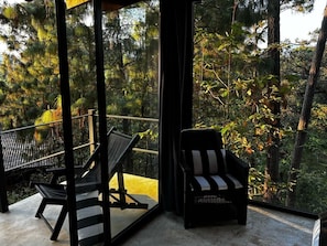 A balcony with a view of a forest, two chairs, and a glass partition. - XOMUE Suite 1 (Valle de Bravo)