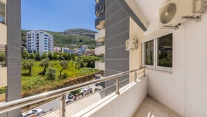 Un balcón con vista a una carretera, coches aparcados y edificios al fondo.