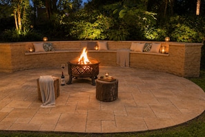 Un patio exterior con una chimenea, asientos y un muro de piedra.