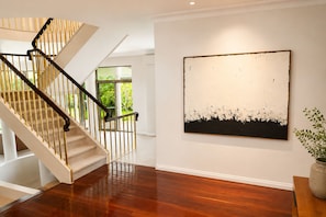 Una escalera con escalones de madera y barandilla metálica, un cuadro abstracto grande en la pared y una planta en maceta sobre una mesa.