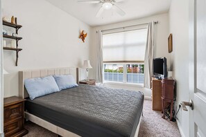 Ein Schlafzimmer mit Bett, Nachttischen, einem Fernseher, einem Fenster mit Vorhängen und einem Deckenventilator.