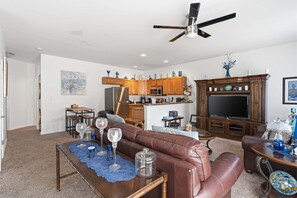 Ein Wohnzimmer mit braunem Ledersofa, ein Essbereich mit Tisch und Stühlen, eine Küche mit Holzschränken und Geräten sowie ein Deckenventilator.