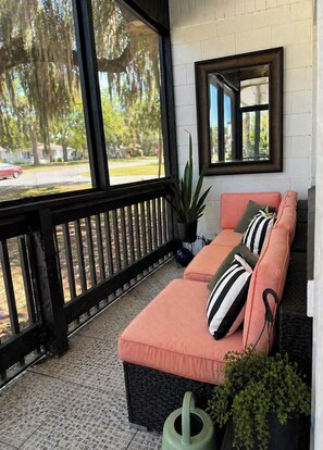 A covered porch with a cushioned seating area, a potted plant, and a large window offering a view of the outdoors. - Cozy Mod Escape, Sleeps 7,  "Oak Tree House" in Clermont Florida (Clermont)