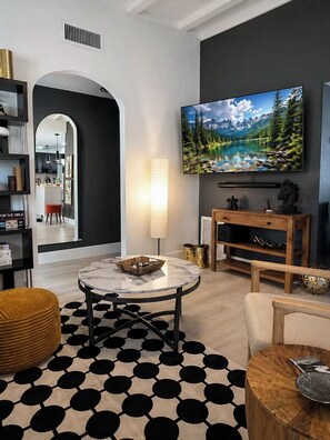 A modern living room with a round marble table, a black and white patterned rug, a large flat-screen TV on the wall, and a wooden entertainment unit. - Cozy Mod Escape, Sleeps 7,  "Oak Tree House" in Clermont Florida (Clermont)