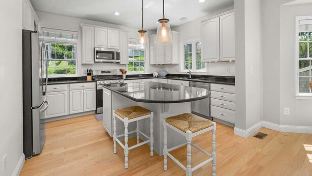 Cocina moderna con armarios blancos, una isla grande, dos taburetes de bar e iluminación colgante.