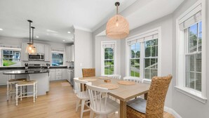 Una cocina moderna con armarios blancos, una isla central y un comedor con mesa de madera y sillas de mimbre.