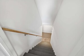 Eine schmale Treppe mit weißen Wänden, einem hölzernen Handlauf und einem Teppichbelag auf dem Podest.