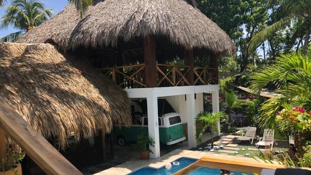 Un área de piscina con una estructura de techo de paja, un edificio blanco y un vehículo verde.