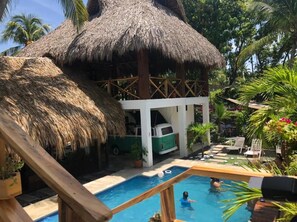 Un área de piscina con una estructura de techo de paja, un edificio blanco y un vehículo verde.