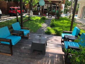 Un patio con mobiliario de madera y una pequeña mesa, rodeado de un jardín y una piscina.
