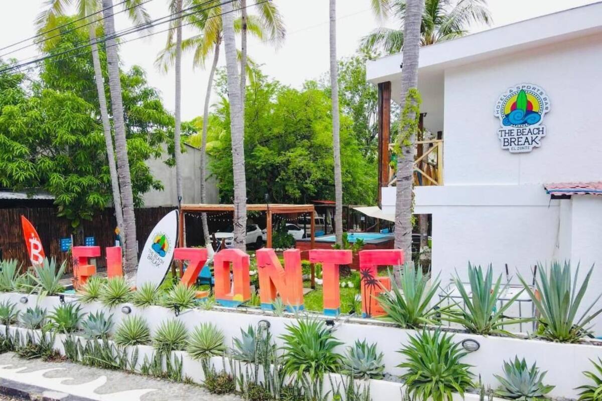 Un hotel llamado 'EL ZONTE' con un letrero, rodeado de plantas tropicales y palmeras.