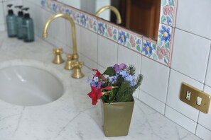 Ein Badezimmer mit Waschbecken, goldenen Wasserhähnen, einer Blumenvase und einer gefliesten Rückwand mit floralen Mustern.