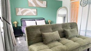 A green sofa in a room with teal walls, a bed with a headboard, and two lamps on nightstands. - 1 Bed - Sleeps 4 - WiFi & Free Parking (Redhill)