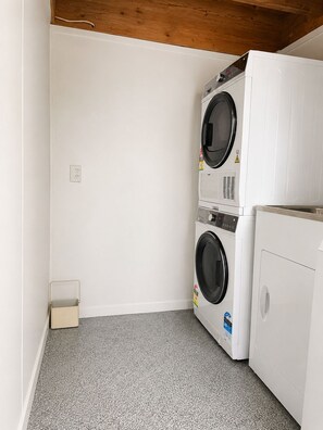 A laundry room with two stacked washing machines and a dryer, a small storage box, and a power outlet on the wall. - Entire home in Greenlane (Auckland)
