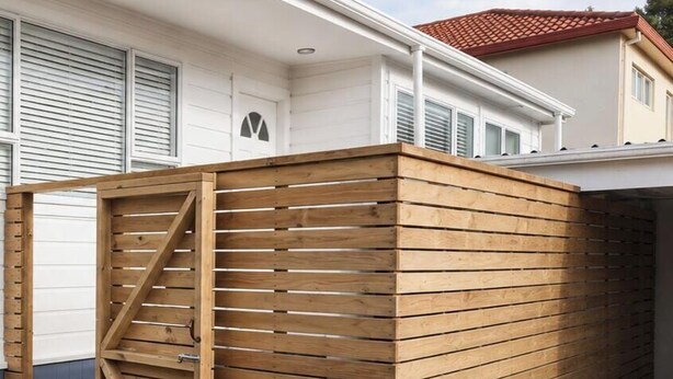 A wooden fence with a gate, a garage door, and a house with a red roof. - Entire home in Greenlane (Auckland)