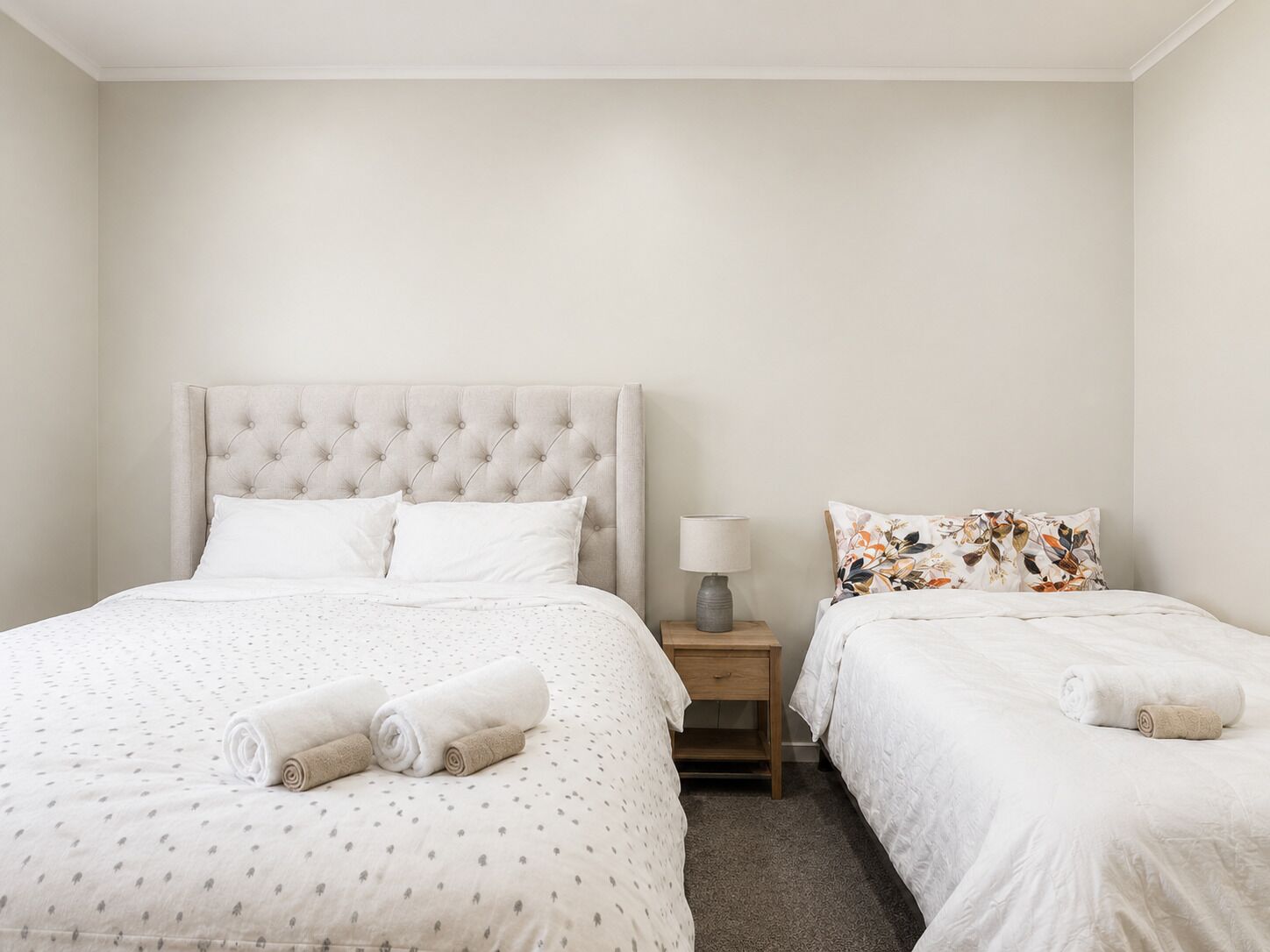 A hotel room with a large bed, a smaller bed, a nightstand with a lamp, and two rolled towels.