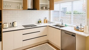 A modern kitchen with white cabinets, a stainless steel dishwasher, and a window with blinds. - Entire home in Greenlane (Auckland)