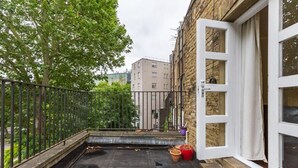 Eine Dachterrasse mit Metallgeländer, einer Tür und Kübelpflanzen.