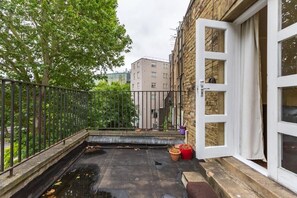 Eine Dachterrasse mit Metallgeländer, einer Tür und Kübelpflanzen.