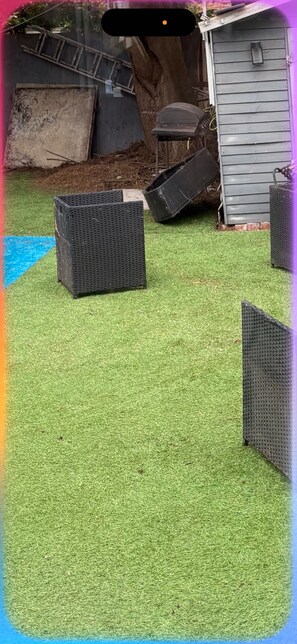 Een achtertuin met kunstgras, een ladder, een tuinhuisje en tuinmeubilair.