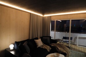 Una habitación con un sofá de color oscuro, una mesita con una taza y una ventana con cortinas.
