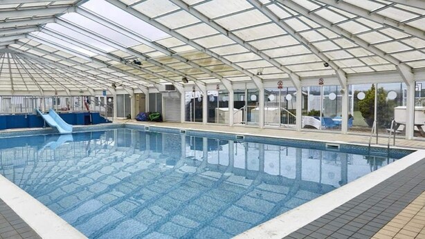 Ein Hallenbad mit Glasdecke, einer Rutsche und einer Sitzgelegenheit.