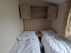 Eine kleine, einfache Unterkunft mit zwei Einzelbetten, einem Holzschrank und einem Fenster mit kariertem Vorhang.