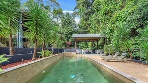 Ein rechteckiger Pool mit klarem Wasser, umgeben von üppiger Vegetation und einem überdachten Sitzbereich.