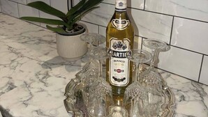 Une bouteille de Martini Bianco posée sur un comptoir en marbre, accompagnée d’un plateau en verre et d’une plante en pot.