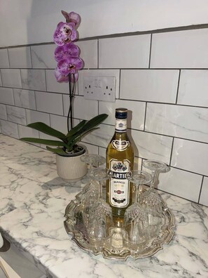 Uma garrafa de Martini Bianco sobre uma bancada de mármore, com um suporte de vidro, uma planta em vaso e uma orquídea roxa.