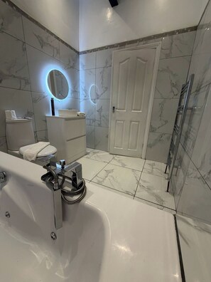 Um banheiro moderno com banheira, vaso sanitário e pia, com azulejos de mármore e box de vidro.
