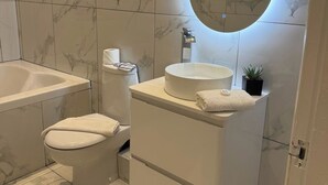Une salle de bain avec une baignoire, des toilettes, un meuble-lavabo avec un miroir et une petite plante en pot.