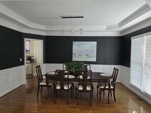 Ein Esszimmer mit dunkler Wand, weißem Zierrahmen, einem Gemälde und einem Esstisch mit Stühlen.