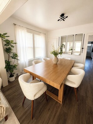 A dining area with a wooden table, white chairs, a potted plant, and a ceiling light fixture. - 4BR Retreat w/ Theater, Arcade, Gym and Firepit (Chicago)