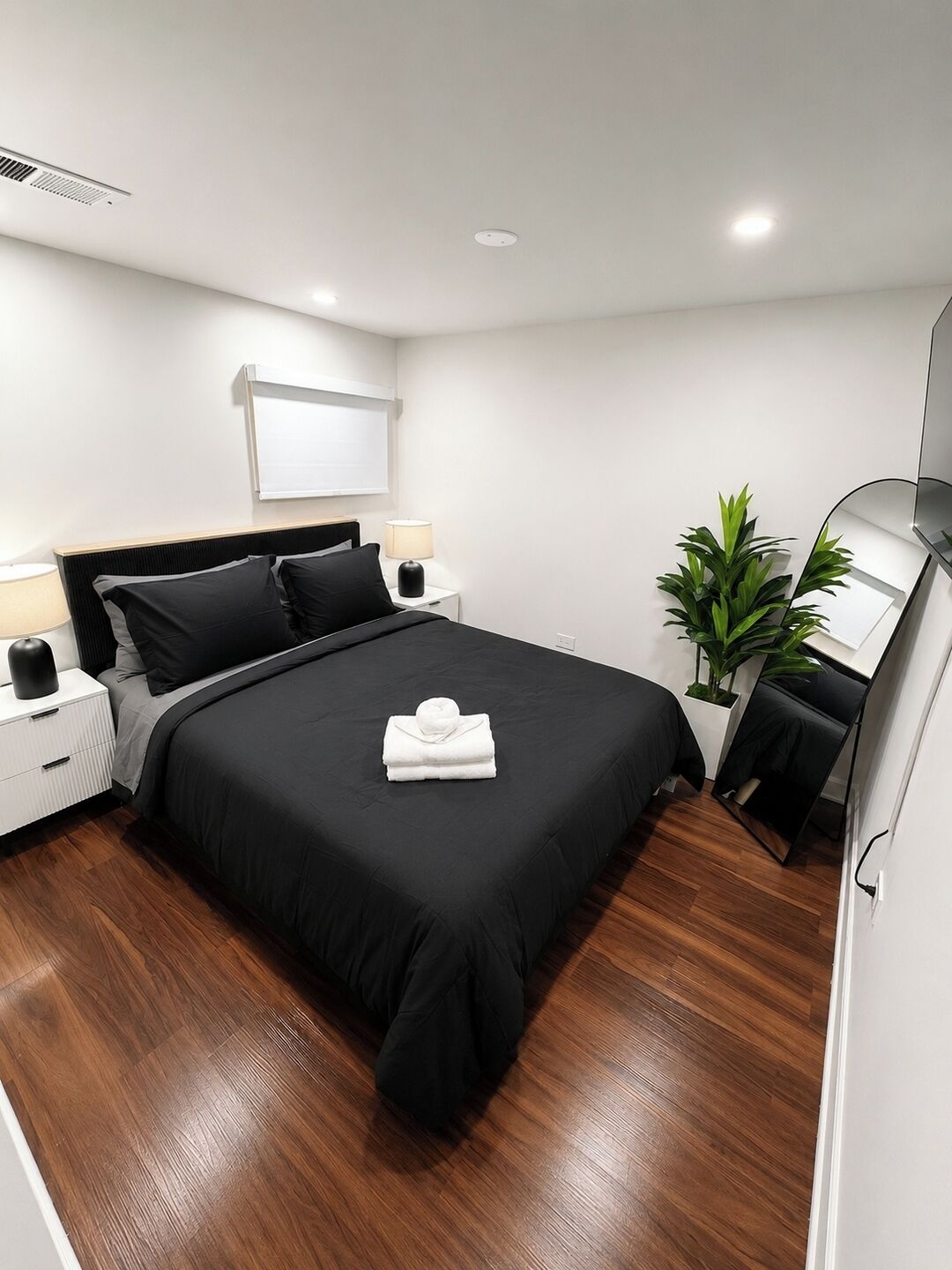 A modern hotel room with a large bed, bedside tables, a mirror, and a potted plant.