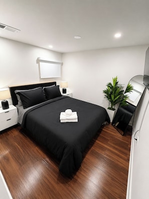A modern hotel room with a large bed, bedside tables, a mirror, and a potted plant.