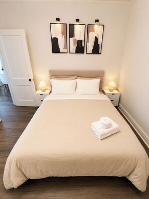 A neatly made bed with a beige bedspread and pillows, two bedside lamps, and three abstract paintings on the wall. - 4BR Retreat w/ Theater, Arcade, Gym and Firepit (Chicago)