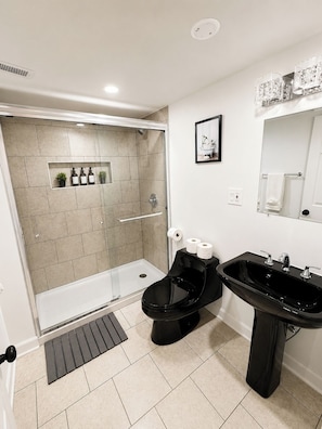 A modern bathroom with a shower, toilet, sink, and a small shelf with toiletries. - 4BR Retreat w/ Theater, Arcade, Gym and Firepit (Chicago)