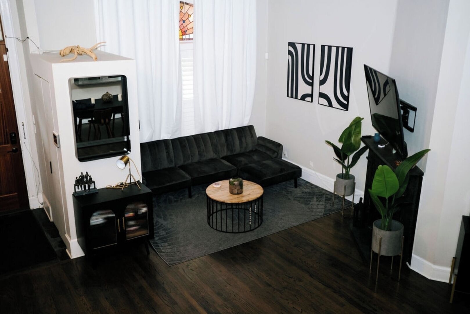 Uma sala de estar moderna com um sofá sectional preto, uma mesa de centro redonda e duas grandes pinturas abstratas na parede.