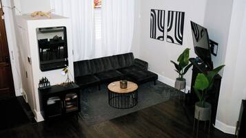 Uma sala de estar moderna com um sofá sectional preto, uma mesa de centro redonda e duas grandes pinturas abstratas na parede.