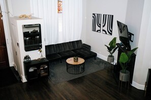 Ein modernes Wohnzimmer mit einem schwarzen Ecksofa, einem runden Couchtisch und zwei großen abstrakten Bildern an der Wand.