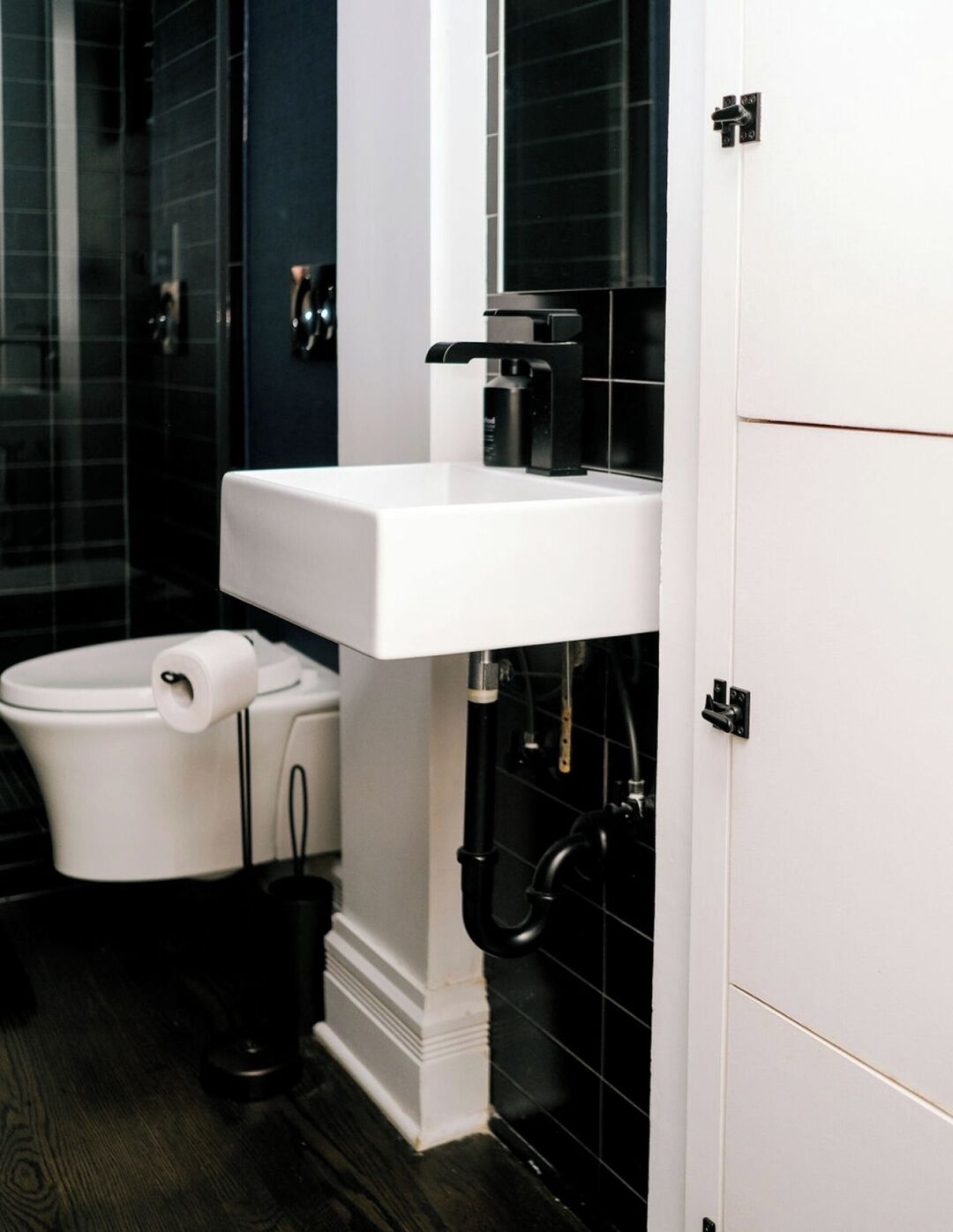 Ein modernes Badezimmer mit einem weißen Waschbecken, einer schwarzen Toilette und dunkel gefliesten Wänden.