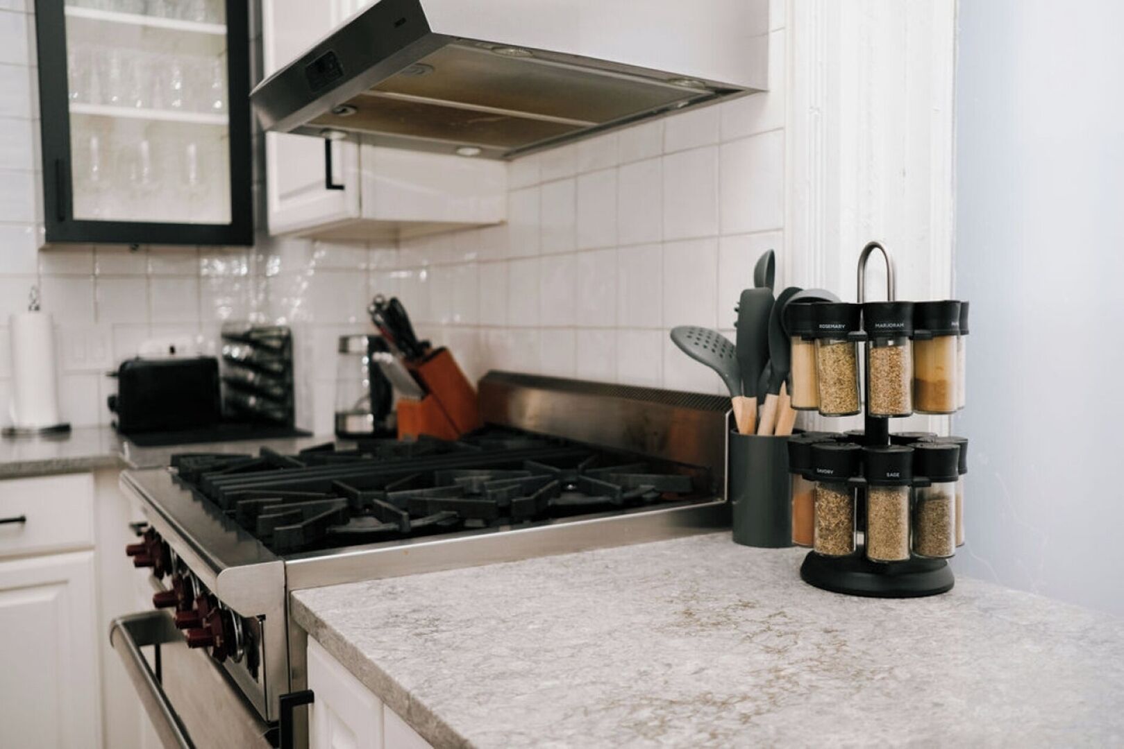 Uma cozinha com fogão a gás, coifa e prateleira de temperos com recipientes.