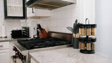 Uma cozinha com fogão a gás, coifa e prateleira de temperos com recipientes.