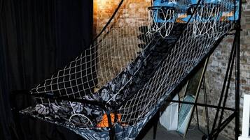 Uma cesta de basquete com rede, montada em ambiente interno com parede de tijolos ao fundo.