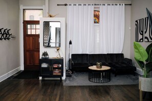 Ein Wohnzimmer mit dunklem Holzboden, einem schwarzen Sofa, einem runden Couchtisch und einer schwarzen Kommode mit Spiegel.