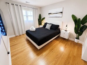 Ein Schlafzimmer mit Bett, Nachttischen, einem Topf mit Pflanze und einem Fenster mit Vorhängen.