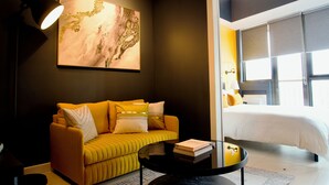 Moderni hotellihuone, jossa on sohva, sohvapöytä, sänky ja suuri ikkuna.